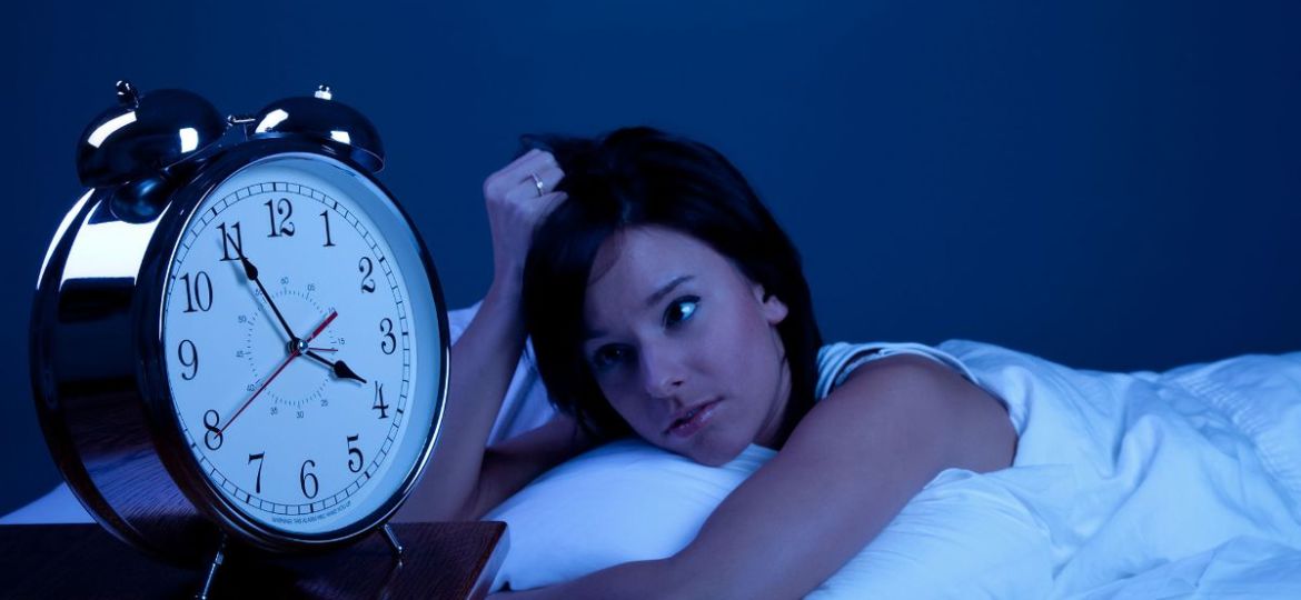 woman in bed looking tiredly at clock