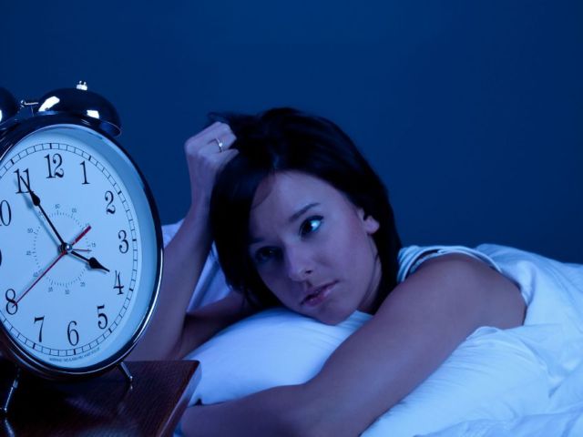 woman in bed looking tiredly at clock